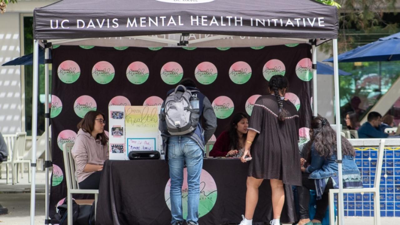 Student surround the Mental Health Initiative table for Mental Health Awareness Month activities.