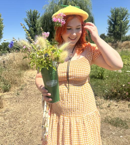 Portrait of Alyssa Reid in a yellow dress holding flowers in a vase with a nature background