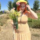 Portrait of Alyssa Reid in a yellow dress holding flowers in a vase with a nature background