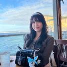 Portrait photo of Elaine He sitting at a table with the ocean in the background